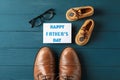Brown leather shoes, children`s shoes, inscription happy fathers day, and glasses on wooden background
