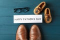 Brown leather shoes, children`s shoes, inscription happy fathers day, and glasses on wooden background