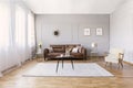 Brown leather sofa in living room interior with stylish armchair, coffee table and drawings