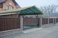 Brown metal gate with a black forged pattern and a long fence of wooden boards