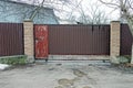 Brown metal gate and red closed door on a fence made of iron