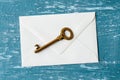 Brown metal shabby vintage key on a white envelope over a turquoise scratched paint surface. Send or receive a key in an envelope