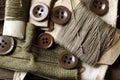 BROWN MILITARY STYLED BUTTONS SCATTERED ACROSS, KHAKI CLOTH, NEEDLES AND THREAD WOUND AROUND PIECES OF CARD
