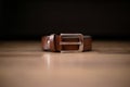 Brown new leather belt with silver buckle positioned on a light brown table with dark background Royalty Free Stock Photo