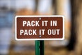 a brown, pack it in, pack it out sign with white lettering and white boarder