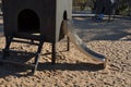 Brown painted wooden house on a playground with a sandpit. stainless steel slides shine in the sandy beach. wooden benches separat Royalty Free Stock Photo