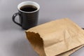 A brown paper bag and a cup of coffee on gray. A full cup of hot, invigorating drink. A lunch bag of food. Selective focus