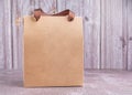 Brown paper bag packaging with ribbon handles placed on a gray stone background with a wooden wall. Side view with copy space for Royalty Free Stock Photo