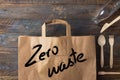 Brown paper grocery shopping bag with zero waste lettering wooden cutlery glass bottle on wood background. Plastic-free