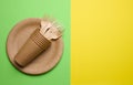 Brown paper plate, stack cups and wooden fork, disposable tableware on green background, top view. Copy space