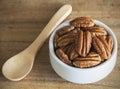 Brown pecans in white Bowl on a wood table.