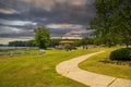 A brown pergola in the park surrounded by lush green trees, grass and plants with a blue lake and a smooth winding footpath Royalty Free Stock Photo