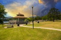 A brown pergola in the park surrounded by lush green trees, grass and plants with a blue lake and a smooth winding footpath Royalty Free Stock Photo