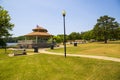 A brown pergola in the park surrounded by lush green trees, grass and plants with a blue lake and a smooth winding footpath Royalty Free Stock Photo