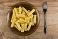 Brown plate with cooked pasta, fork on table. Top view