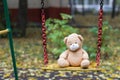 Brown plush teddy bear on a yellow colourful swing.