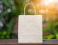 Brown recyclable paper shopping bag Placed on a wooden table, the backdroup is a green tree.