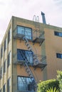 Brown and red brick building with metal saftey fire ladder and front yard trees and foliage in part shade and sun