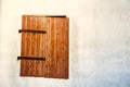 Brown red wooden window with rusted metal hinges on a white cement wall detail.