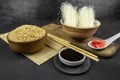 Brown rice in a wooden bowl, asian kitchen background with bamboo mat, chopsticks, soy sauce and glass rice noodles on black Royalty Free Stock Photo