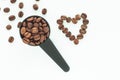 Brown roasted coffee beans in a black measuring spoon on a white background isolated