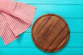 Brown round cutting board for pizza on red plaid tablecloth. Blue wooden background in the restaurant. copy space. Top view. Royalty Free Stock Photo