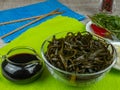 Brown seaweed in a transparent bowl, a glass gravy boat with soy sauce, plates with chopped onions, parsley, dill, red