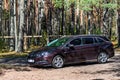 Brown shiny german car Opel Astra ST parked in quiet forest roadside on blurred bokeh background on bright sunny day