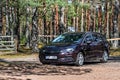 Brown shiny german car Opel Astra ST parked in quiet forest roadside on blurred bokeh background on bright sunny day