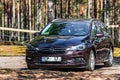 Brown shiny german car Opel Astra ST parked in quiet forest roadside on blurred bokeh background on bright sunny day