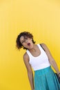 Brown-skinned girl in casual dress gesturing effusively on a yellow wall. Space for text