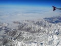 Brown snowy mountains under the clouds and blue sky. View from the airplane window. Gray wing of an airplane Royalty Free Stock Photo