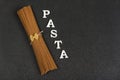 Brown spelt spaghetti on gray background and the word Pasta. Dry spaghetti. Italian cuisine