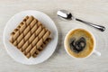 Brown wafer rolls with chocolate filling in plate, spoon, black coffee in cup on wooden table. Top view Royalty Free Stock Photo