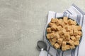 Brown sugar cubes in bowl and spoon on light grey table, flat lay. Space for text Royalty Free Stock Photo