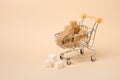 Brown sugar cubes in a miniature shopping trolley on a beige background, useful and harmful sugar concept, copy space