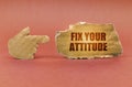 On a brown surface, a cardboard hand points to a sign that says - Fix Your Attitude
