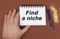 On a brown surface are coins, a pen and a notepad with the inscription - Find a niche