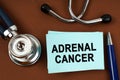 On a brown surface there is a stethoscope, a pen and blue stickers with the inscription - adrenal cancer