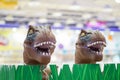 2 brown t-rex model toys head up from plastic grass in the kids shop, Bangkok department store, Thailand