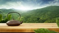 A brown teapot on wooden table with beautiful green trees mountains and blue cloudy sky background. Royalty Free Stock Photo
