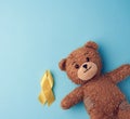 Brown teddy bear holds in his paw a yellow ribbon folded in a loop on a blue background. concept of the fight against childhood Royalty Free Stock Photo