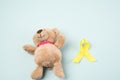 Brown teddy bear holds in his paw a yellow ribbon folded in a loop on a blue background Royalty Free Stock Photo