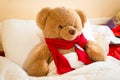 Brown teddy bear in read scarf lying in bed with thermometer Royalty Free Stock Photo
