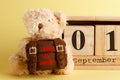 Brown teddy bear with school backpack and decoratibe wooden calendar, yellow background