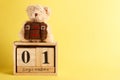 Brown teddy bear with school backpack and decoratibe wooden calendar, yellow background