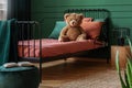 Brown teddy bear on single metal bed with burn orange and emerald green bedding