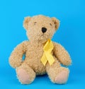 brown teddy bear sits and holds in his paw a yellow silk ribbon on a blue background Royalty Free Stock Photo