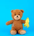 brown teddy bear sits and holds in his paw a yellow silk ribbon on a blue background Royalty Free Stock Photo