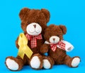 Brown teddy bear sits and holds in his paw a yellow silk ribbon on a blue background, concept of the fight against childhood Royalty Free Stock Photo